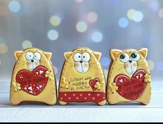 three yellow cats with red hearts on their backs, one is holding a heart shaped cookie