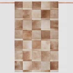 an area rug with squares in brown and beige colors on a white background, hanging from a wooden frame