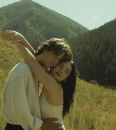 two people embracing each other in the middle of a field with mountains in the background