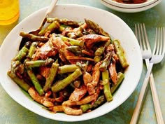 a white bowl filled with chicken and asparagus next to two glasses of orange juice