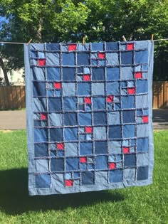 a blue and red quilt hanging on a clothes line in the grass with trees in the background