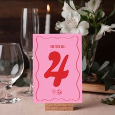 a pink card with the number twenty four in front of some wine glasses and flowers