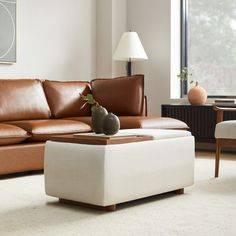 a living room with a couch, ottoman and table in front of a large window