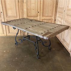 an old wooden table with wrought iron legs in front of wood paneled walls and doors