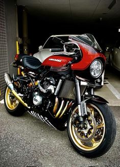 a red and black motorcycle parked next to a silver car in a parking garage area