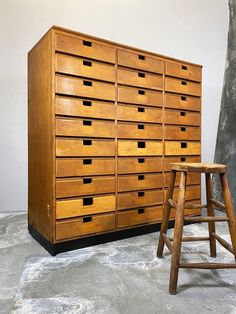 an old wooden dresser with several drawers and a stool next to it on a cement floor