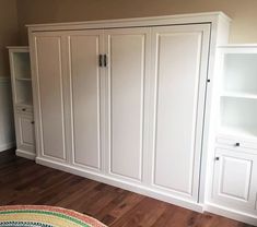 an empty room with white cupboards and shelves on the wall next to a rug