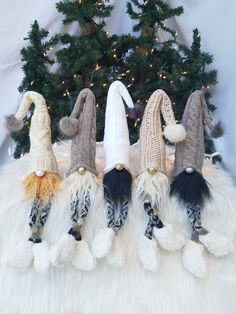 four knitted gnomes are lined up in front of a christmas tree