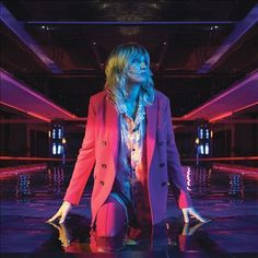 a woman with long hair wearing a red jacket and purple pants standing in an empty room