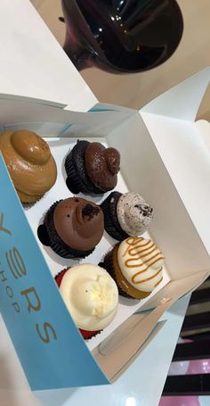 a box filled with different types of cupcakes on top of a white table