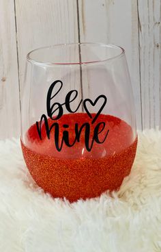 a wine glass with the words bee mine painted on it sitting on a white rug