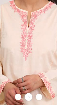 a woman wearing a white shirt with pink embroidery on it