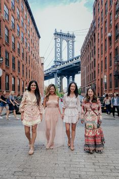 three women are walking down the street in front of some tall buildings and a bridge