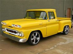 an old yellow pickup truck parked in front of a building