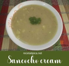 a white bowl filled with soup sitting on top of a table next to a red and green place mat