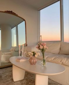 a white table with flowers and candles on it in front of large windows overlooking the ocean