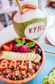 a wooden bowl filled with fruit and nuts on top of a blue plate next to a coconut