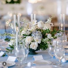 a centerpiece with white flowers and greenery on a table