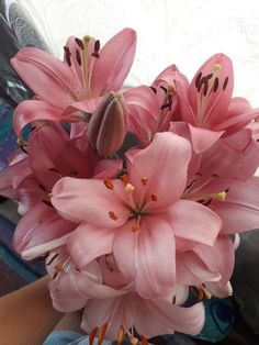 pink flowers are in a glass vase on the table next to a person's arm