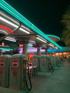 gas pumps are lined up in front of a building with neon lights on the roof