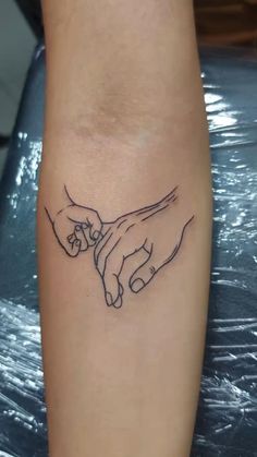 two hands holding each other on the wrist tattoo design for men and women, done in black ink