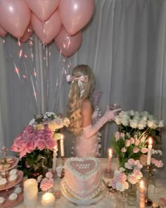 a woman standing in front of a table filled with pink and white cakes, candles and balloons