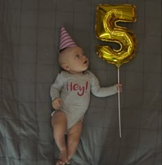 a baby is laying down with a number five balloon