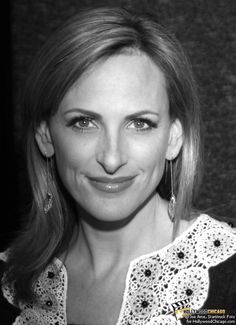 a black and white photo of a woman with large earrings on her head, smiling at the camera