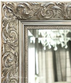 an ornate silver framed mirror with a chandelier in the background