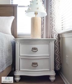 a white lamp sitting on top of a nightstand next to a bed