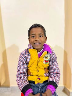 a young boy sitting on top of a red chair wearing a yellow vest and purple mitts