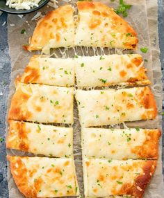 sliced pizza sitting on top of a piece of parchment paper next to a bowl of cheese