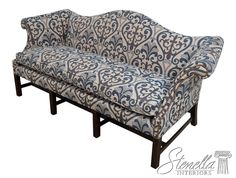 a blue and white patterned couch sitting on top of a wooden frame with black legs