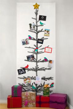 a small christmas tree with pictures on it and wrapped presents under the tree, in front of a white wall