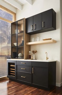 a kitchen with black cabinets and wooden flooring next to a window overlooking the water