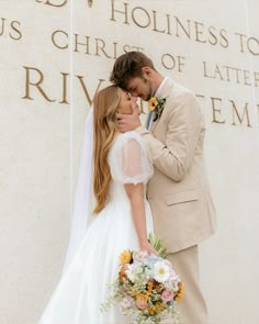 a bride and groom kissing in front of the lincoln memorial with flowers on their bouquet