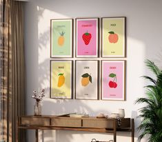 four framed fruit posters hanging on the wall above a table in front of a potted plant