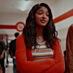 a woman standing with her arms crossed in a room full of people and looking off into the distance