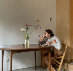 a woman sitting at a table eating food and flowers in a vase on top of the table