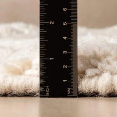 a close up of a measuring ruler on a white rug with wool in the background