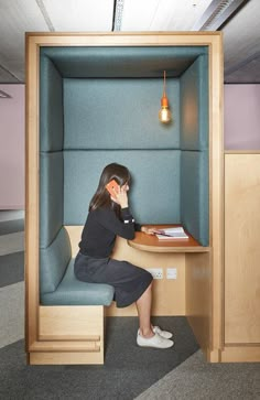 a woman sitting at a desk in an office cubicle with a phone to her ear