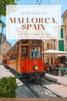 an orange trolley car traveling down the street with people sitting at tables and umbrellas