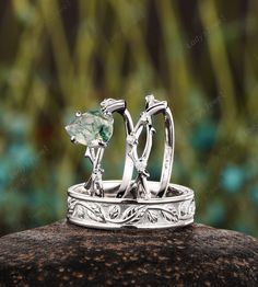 two wedding rings with an emerald stone in the middle on top of a rock outside