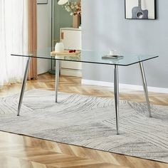 a glass table with metal legs in front of a blue wall and wooden flooring