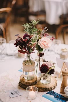 two vases filled with flowers on top of a wooden slice at a wedding reception