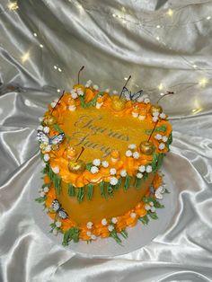 a birthday cake decorated with orange flowers and butterflies is on a white tablecloth covered surface