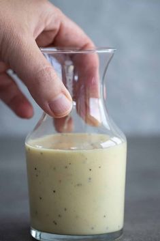 a person is dipping something into a small glass container with liquid in it and another hand reaching for the top