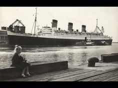 a woman sitting on a dock next to a large ship