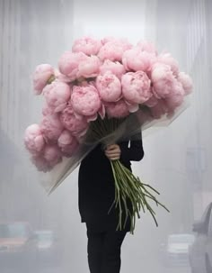 a man holding a bunch of pink flowers in his hand while walking down the street