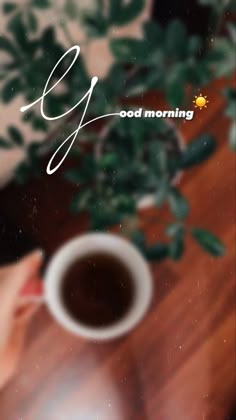 a cup of coffee sitting on top of a wooden table next to a potted plant